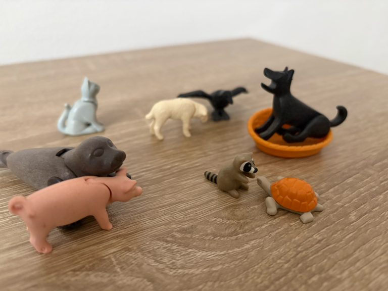 Spielzeugtiere: Hunde, Katzen, Schwein und eine Schildkröte auf einem Tisch angeordnet.