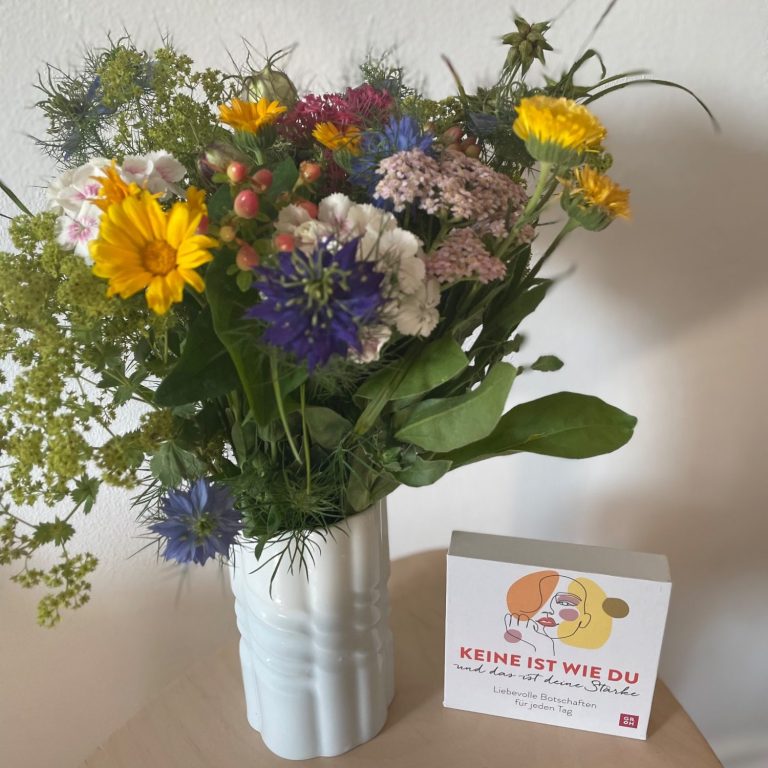 Bunte Blumen in einer weißen Vase neben einer Karte mit illustrativen Figuren.
