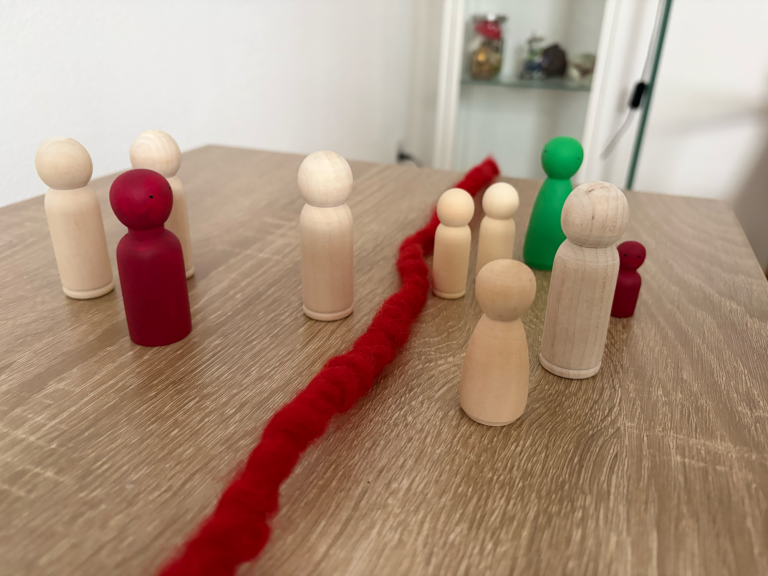 Bunte Holzfiguren auf einem Tisch, einige hinter einer roten Schnur angeordnet.