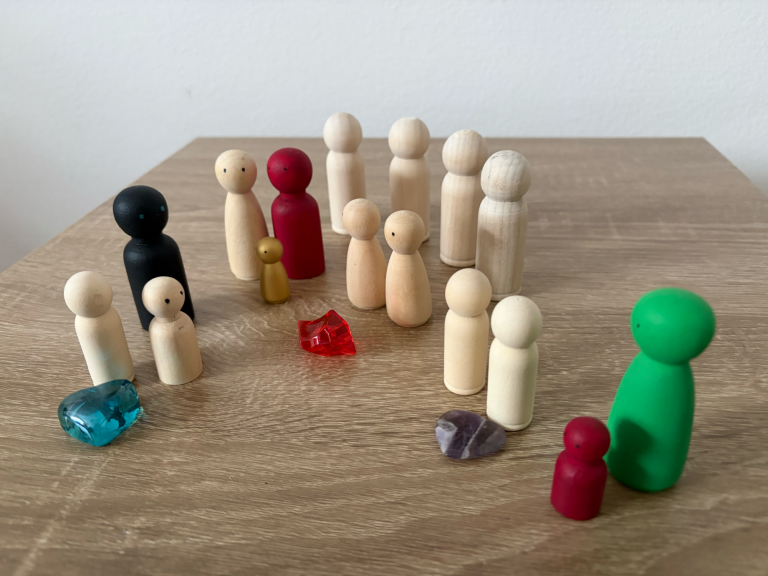 Bunte Holzfiguren versammelt um bunte Glassteine auf einem Holzuntergrund.