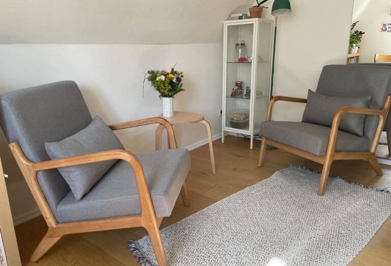 Zwei moderne Sessel mit Holzgestell, Tisch und Blumen in einem hellen Raum.