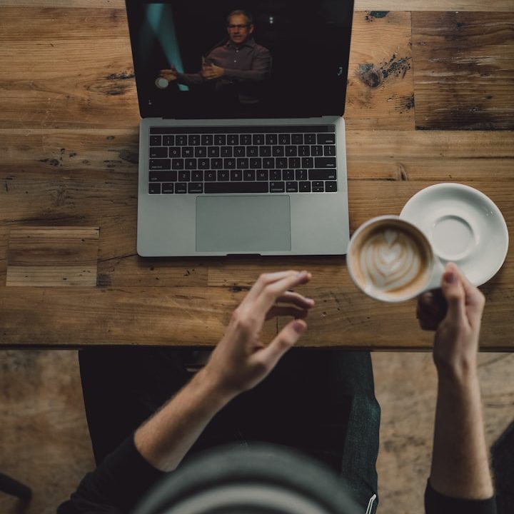 Eine Person hält eine Tasse Kaffee, während sie auf einen Laptop blickt.